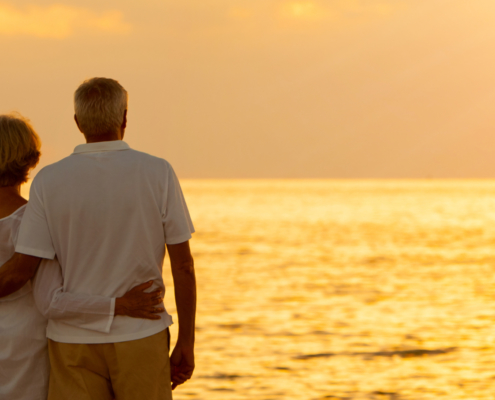 Panorama senior man and woman couple embracing at sunset or sunrise on a deserted tropical beach panoramic web banner