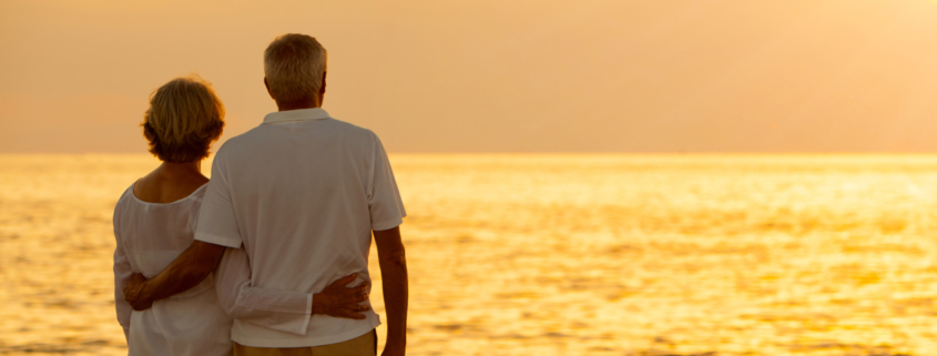 Panorama senior man and woman couple embracing at sunset or sunrise on a deserted tropical beach panoramic web banner