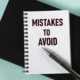 MISTAKES TO AVOID - words in a white notebook against the background of a black notebook with a pen. Business concept