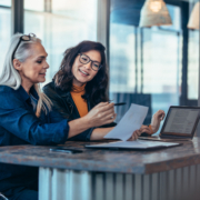 Two women analyzing documents while sitting on a table