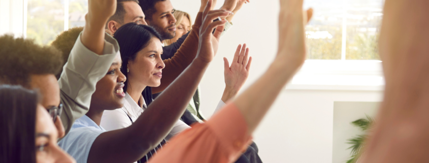 Group of people sitting down raising their hands